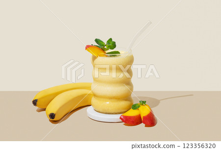 Smoothie with mango and banana in a glass on a yellow background with fruits and shadow. 123356320