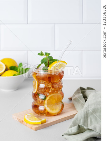 Iced tea with lemon, ice and mint in a glass on the kitchen countertop with citrus fruits Iced tea with lemon, ice and mint in a glass on the kitchen countertop with citrus fruits 123356326