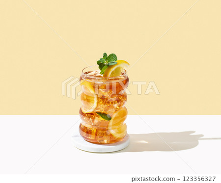 Iced tea with lemon, ice and mint in a glass on white and yellow background with shadow. 123356327