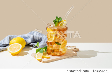 Iced tea with lemon, ice and mint in a glass on beige and white background with shadow 123356330