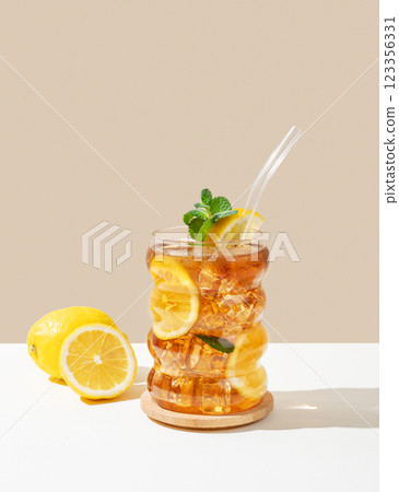 Iced tea with lemon, ice and mint in a glass on a white and beige background with shadow. 123356331
