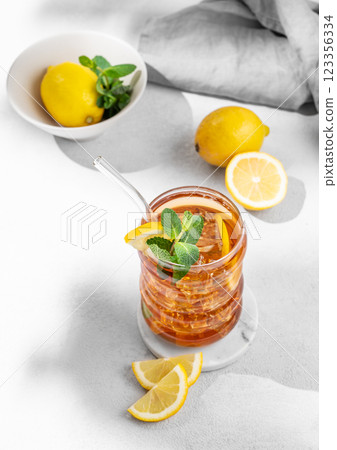 Iced tea with lemon, ice and mint in a glass on light  background with shadow, citrus fruits  123356334