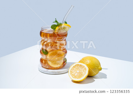 Iced tea with lemon, ice and mint in a glass on white and blue background with shadow. 123356335