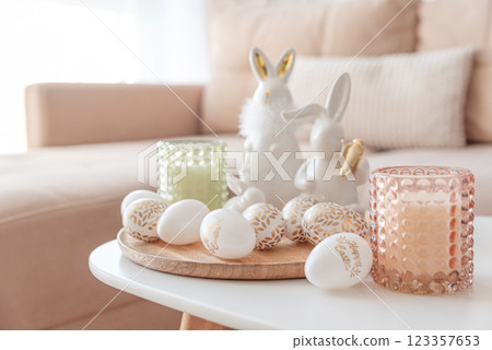Easter eggs, candles and white ceramic rabbits on wooden table in interior of living room Easter eggs, candles and white ceramic rabbits on wooden table in interior of living room 123357653