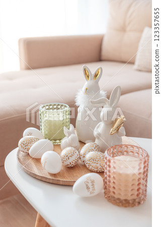 Easter eggs, candles and white ceramic rabbits on wooden table in interior of living room 123357655
