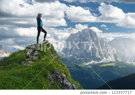 Girl on the mountain peak with yellow flowers and green grass Girl on the mountain peak with yellow flowers and green grass 123357717
