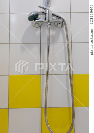 A modern showerhead complements the bright, inviting yellow tiled wall in a stylish bathroom A modern showerhead complements the bright, inviting yellow tiled wall in a stylish bathroom 123359445