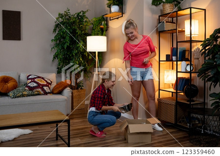 Women joyfully unbox new decor items in a living room, celebrating creativity and warmth 123359460