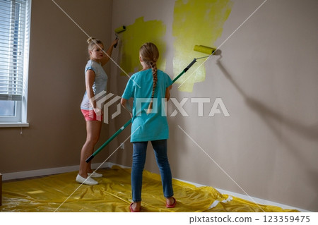 Two Young Children Thoroughly Enjoy Painting a Wall with a Bright, Cheerful Yellow Color 123359475