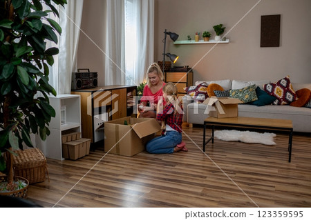In her charming and cozy living room, a woman is carefully unpacking boxes filled with items In her charming and cozy living room, a woman is carefully unpacking boxes filled with items 123359595