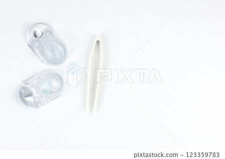 Two disposable contact lens containers and a contact blue soft lens and beige tweezers lie on the left on a white background in close-up with space for text. The concept of ophthalmology, vision 123359783