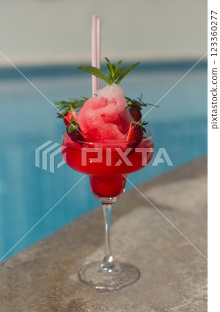beautiful red cocktail with pieces of strawberries and straws on the background of the pool 123360277