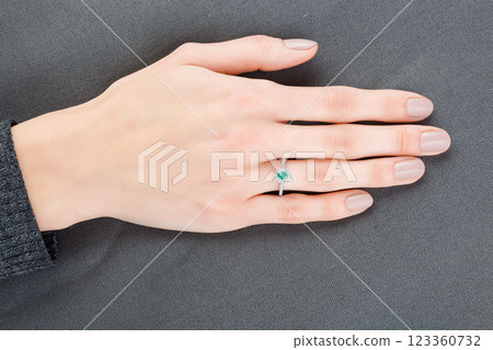 Beautiful female hand with gold ring with diamonds and emerald on gray background Beautiful female hand with gold ring with diamonds and emerald on gray background 123360732