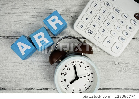 ARR (Annual Recurring Revenue) text with alarm clcok and calculator on wooden background 123360774
