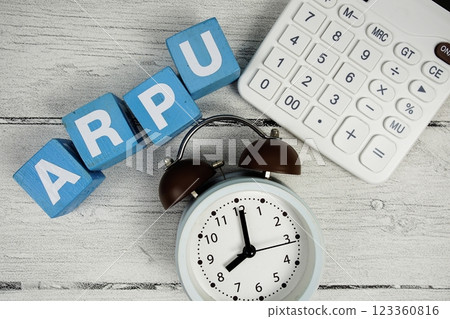 ARPU (Average Revenue Per User) text with alarm clock and calculator on wooden background 123360816