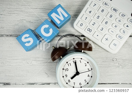 SCM (Supply Chain Management) text with alarm clock and calculator on wooden background 123360937