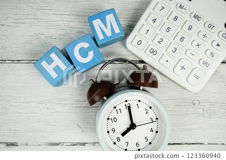 HCM (Human Capital Management) text with alarm clock and calculator on wooden background HCM (Human Capital Management) text with alarm clock and calculator on wooden background 123360940