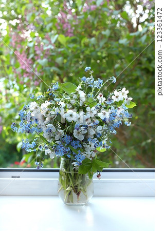 Home interior with decor elements, beautiful spring cherry branches and forget-me-nots in a vase on a sunny window, abstract flower composition, still life with place for text, floral card for Home interior with decor elements, beautiful spring cherry branches and forget-me-nots in a vase on a sunny window, abstract flower composition, still life with place for text, floral card for 123361472