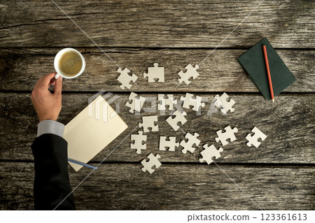 Businessman reaching for a cup of coffee on his rustic wooden desk as he searches for solution to a problem 123361613
