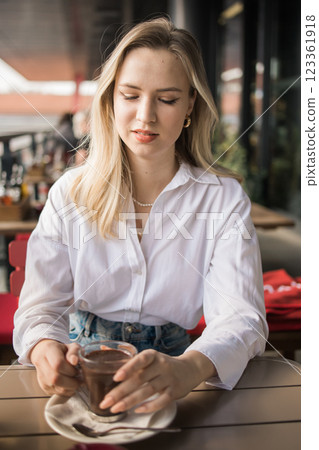 Gen z blonde woman drinks hot chocolate in summer cafe. Tasty beverage and break concept. Generation z people 123361918