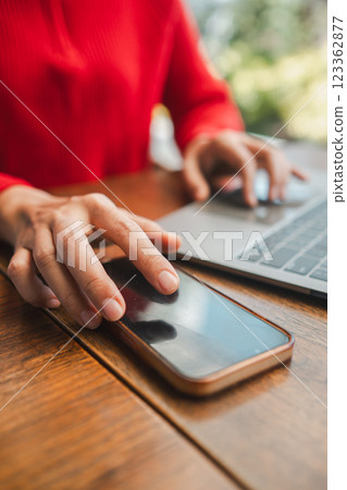 Hands interacting with smartphone and laptop on a wooden table, showcasing modern technology and connectivity. 123362877