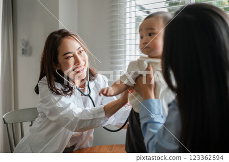 Pediatrician uses stethoscope to check baby's health while parent holds child in a bright medical office. 123362894