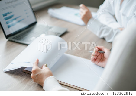 Professionals engaged in a business meeting, reviewing documents and analyzing data on a laptop in a modern office environment. 123362912