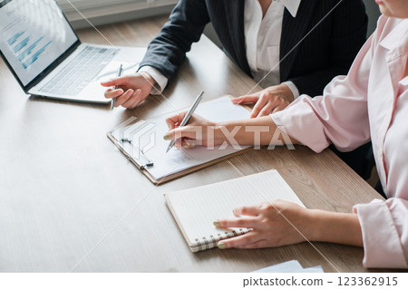 Two professionals collaborating in a modern office, analyzing data on a laptop and taking notes during a business meeting. 123362915
