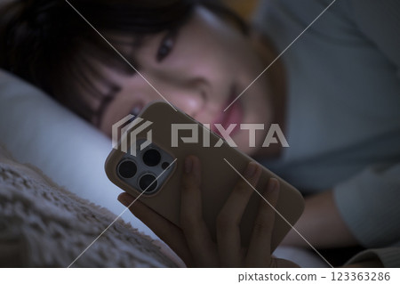 一名婦女在床上的看一個智能手機 123363286