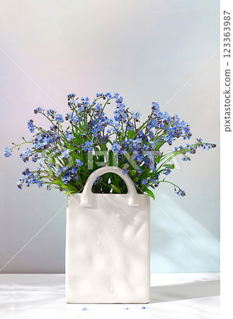Beautiful spring forget-me-not flowers in a vase on a light background, flyer. Abstract flower arrangement, still life with space for text, floral holiday card, summer greeting concept, selective 123363987