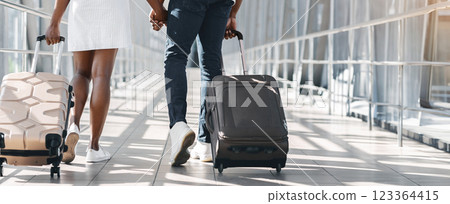 A couple walks together through an airport terminal, both pushing their luggage behind them. The woman is wearing a white dress and the man is wearing jeans and a dark shirt, back view A couple walks together through an airport terminal, both pushing their luggage behind them. The woman is wearing a white dress and the man is wearing jeans and a dark shirt, back view 123364415