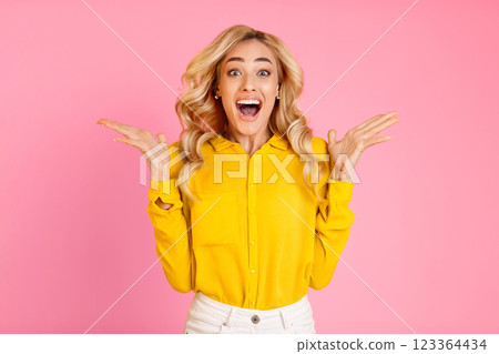 A young woman with blonde hair is standing in front of a pink background. She is wearing a yellow button-down shirt and white pants A young woman with blonde hair is standing in front of a pink background. She is wearing a yellow button-down shirt and white pants 123364434