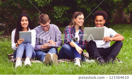 University students with devices preparing for classes, having break in campus, sitting on grass University students with devices preparing for classes, having break in campus, sitting on grass 123364610