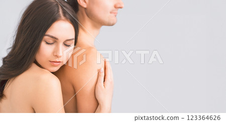 A woman with long dark hair is embracing a man from behind. She has her eyes closed and her head resting on his shoulder. Both are bare-chested and appear to be intimate, copy space 123364626