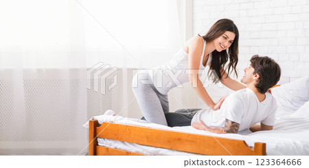 Cheerful young woman cuddling with her man in bed. Loving couple have fun at home, hugging and smiling, copy space 123364666