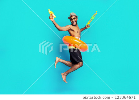African American man is jumping in the air with a big smile on his face. He is wearing a hat, sunglasses, and swim trunks. He is holding a yellow and green water gun in each hand 123364671