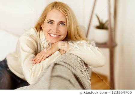 Lovely Middle-Aged Woman With Beaming Smile Sitting On Sofa And Looking At Camera Lovely Middle-Aged Woman With Beaming Smile Sitting On Sofa And Looking At Camera 123364700