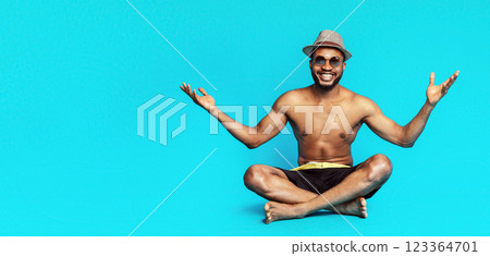A smiling, shirtless black man sits with his legs crossed in a lotus position. He is wearing a straw hat, sunglasses, and black swim trunks. He is looking at the camera with his arms outstretched A smiling, shirtless black man sits with his legs crossed in a lotus position. He is wearing a straw hat, sunglasses, and black swim trunks. He is looking at the camera with his arms outstretched 123364701