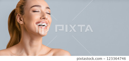 Woman with long blonde hair pulled back in a ponytail, smiling with her eyes closed against a gray background. Her bright white teeth are visible as she laughs with genuine happiness, copy space Woman with long blonde hair pulled back in a ponytail, smiling with her eyes closed against a gray background. Her bright white teeth are visible as she laughs with genuine happiness, copy space 123364746