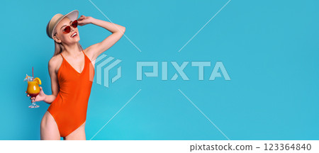 This image features a woman in a red swimsuit, straw hat, and sunglasses, holding a tropical cocktail. She is smiling and looking away from the camera. The background is a solid blue color. This image features a woman in a red swimsuit, straw hat, and sunglasses, holding a tropical cocktail. She is smiling and looking away from the camera. The background is a solid blue color. 123364840
