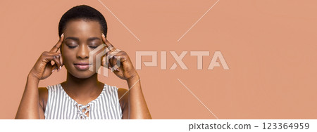African American young woman meditating with her eyes closed. She is touching her temples with her index fingers, indicating relaxation and focus 123364959