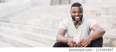 A man sits on some stairs, looking at his phone and smiling. A man sits on some stairs, looking at his phone and smiling. 123364987