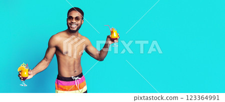 Positive African American shirtless guy holding cocktails and smiling, posing isolated on blue studio background, copy space Positive African American shirtless guy holding cocktails and smiling, posing isolated on blue studio background, copy space 123364991