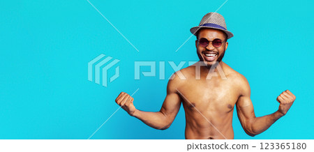 A shirtless African American man with a beard is wearing a straw hat and sunglasses. He is smiling broadly and flexing both arms. The man is standing in front of a bright blue background. A shirtless African American man with a beard is wearing a straw hat and sunglasses. He is smiling broadly and flexing both arms. The man is standing in front of a bright blue background. 123365180