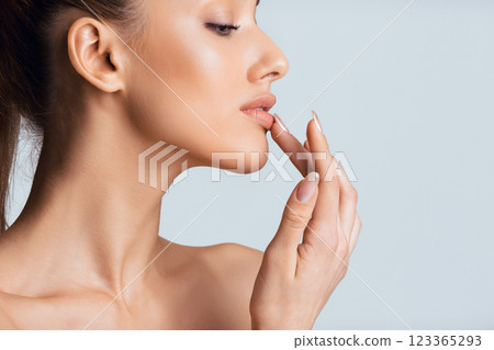 A closeup of a woman face and hand, showing her applying lip balm to her lips with her fingertip. The background is a soft, light blue, copy space A closeup of a woman face and hand, showing her applying lip balm to her lips with her fingertip. The background is a soft, light blue, copy space 123365293