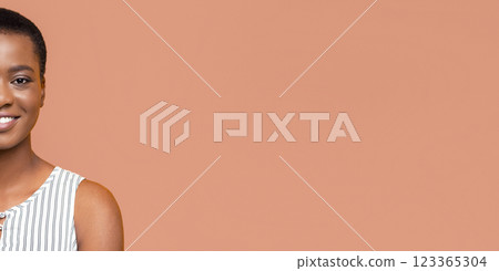 Half face of African American smiling woman with short, dark hair is shown from the shoulders up against a peach-colored background. Half face of African American smiling woman with short, dark hair is shown from the shoulders up against a peach-colored background. 123365304