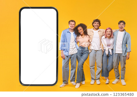 This image features a group of five young friends, including two men and three women, standing together in front of a large smartphone with a white screen. This image features a group of five young friends, including two men and three women, standing together in front of a large smartphone with a white screen. 123365480