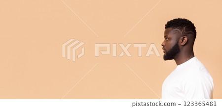 African American man with short, styled hair and a beard. He is wearing a white t-shirt and standing in front of a light peach background, panorama with copy space 123365481