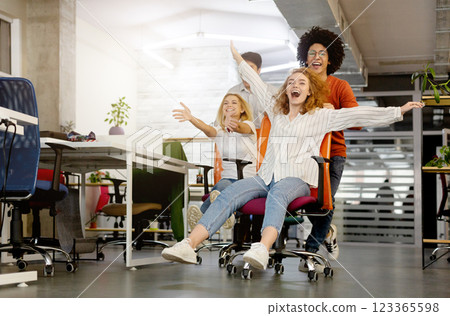 Time for fun. Young cheerful business people racing on office chairs and laughing, free space 123365598