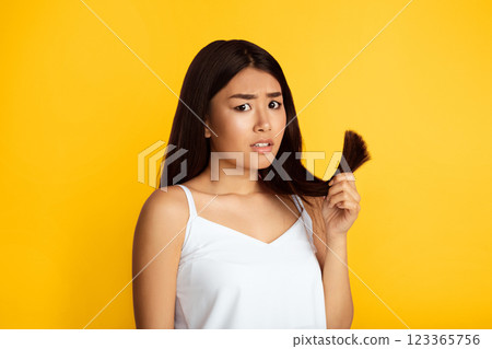 Oh No, Split Hairs. Frustrated Asian Lady Holding Hair Tips On Yellow Studio Background 123365756